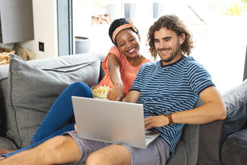 A diverse couple relaxes on sofa with a laptop at home
