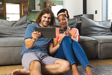 A diverse couple is shopping online with a tablet at home