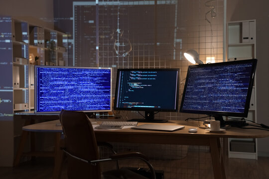 Computer monitors with programming code on table in office at night