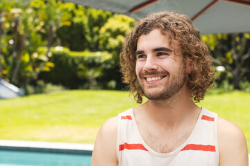 A young Caucasian man smiles warmly near a pool outdoors with copy space at home