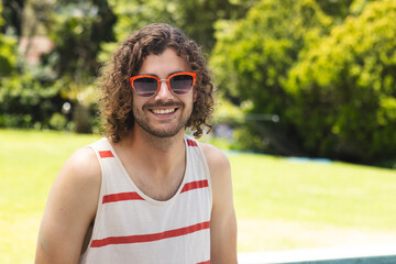 A young Caucasian man with curly hair smiles outdoors with copy space at home