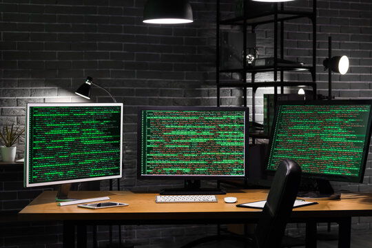 Computer monitors with programming code on desk in office at night
