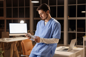 Male nurse with tablet computer working evening shift in clinic