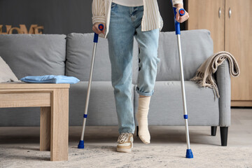 Injured young woman with crutches after accident walking at home