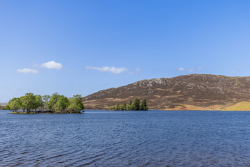Scottish loch embrace an island lush with trees, set against a backdrop of gentle hills. Hidden...