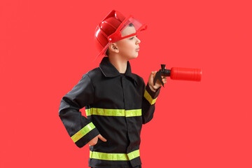 Cute little firefighter with toy extinguisher on red background