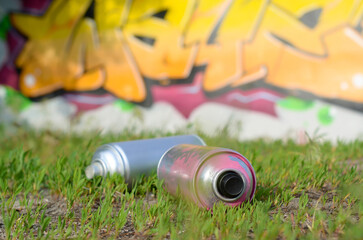 Several used spray cans with paint and caps for spraying paint under pressure on grass near the...
