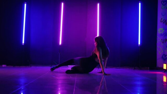 Silhouette of woman dancing under neon lights. Vibrant neon lit dance floor with woman in motion. Energetic dance performance in dark room with neon glow. Ecstatic female dancer surrounded by neon lig