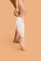 Legs of young woman with soft feather on brown background. Epilation concept
