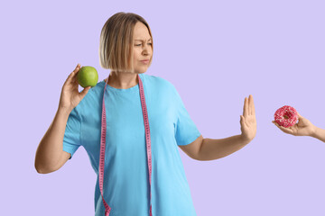 Pretty young woman with apple refusing to eat donut on lilac background. Weight loss concept