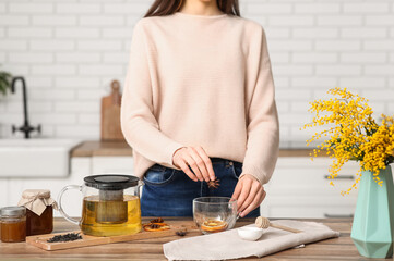 Young woman adding star anise in tea cup in kitchen