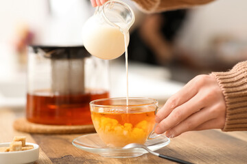 Young woman pouring milk in cup of tea in kitchen