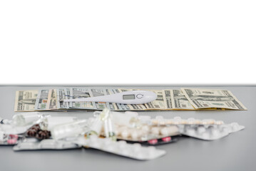 many blisters with pills and ampoules next to spread out dollar banknotes on a gray table with copy space background