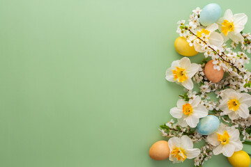 Festive background with spring flowers and Easter eggs, white daffodils and cherry blossom branches on a green pastel background
