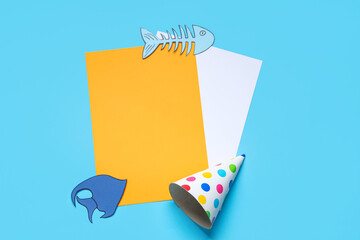Blank card with paper fishes and party hat on blue background. April Fools Day celebration