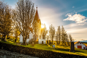 Old wooden white church with cemetery in sunlight. Iceland