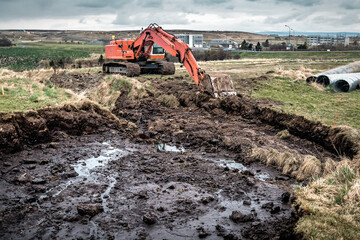 Red excavator digging black soil ground before pipe laying