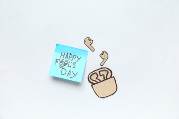 Sticky note and carton earphones on white background. April Fools Day prank