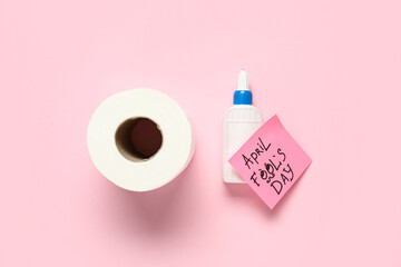 Toilet paper, glue and sticky note on pink background. April Fools Day prank