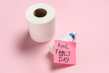 Toilet paper, glue and sticky note on pink background. April Fools Day prank