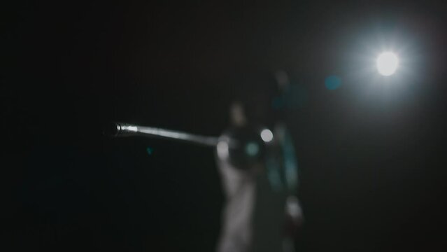 POV footage with focus on rapier tip of unrecognizable foil fencer pointing sword straight to camera while standing on black background with light