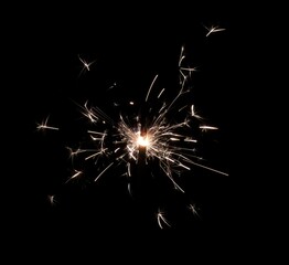 A burning sparkler that shoots hot and bright sparks on a black background