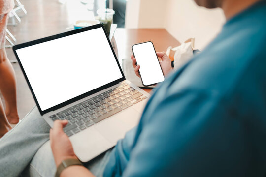 Close-up image of a man sitting in the cafe and using his smartphone and laptop. smartphone and laptop white blank screen mockup for display your graphic banner.