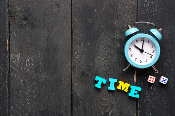 Text TIME with alarm clock and dices on black wooden background. Time management concept. Top view