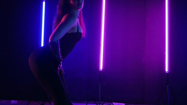 Vibrant neon lit dance floor with woman in motion. Energetic dance performance in dark room with neon glow. Silhouette of woman dancing under neon lights. Ecstatic female dancer surrounded by neon lig
