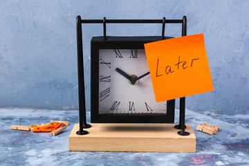 Text LATER with black alarm clock on table against blue background. Time management