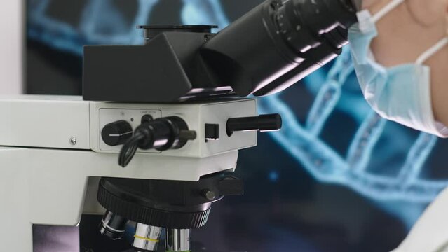 In a modern medical laboratory: a handsome microbiologist in glasses looks into a microscope, analyzing a sample. A brilliant scientist working with high-tech equipment. Close-up