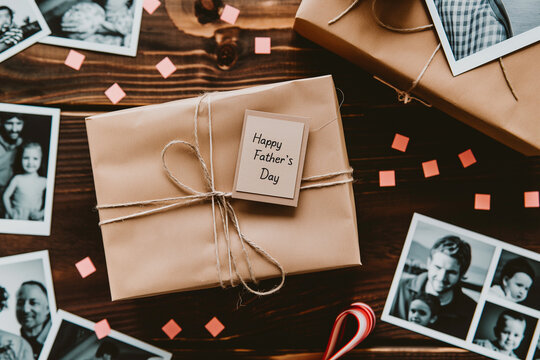 Warm and inviting Father's Day background, close-up of a gift box and a "Happy Father's Day" card on a wooden table, surrounded by family photos