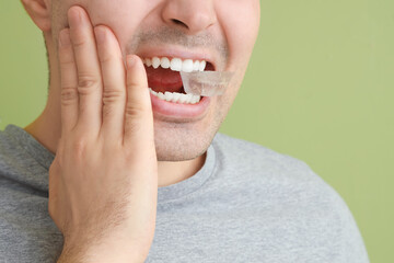 Young man with ice cube suffering from toothache on green background, closeup