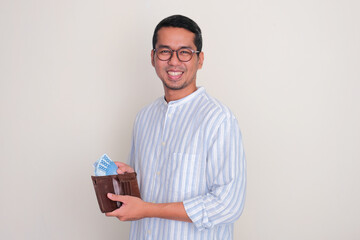 Adult Asian man smiling happy while taking money from inside a wallet