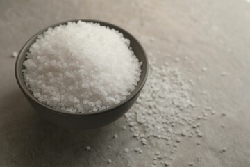 Natural salt in bowl on grey table, space for text