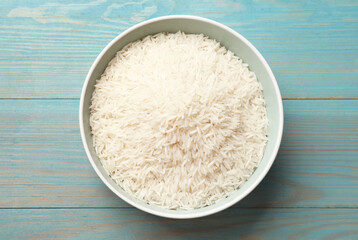Raw basmati rice in bowl on light blue wooden table, top view