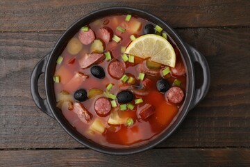 Meat solyanka soup with thin dry smoked sausages in bowl on wooden table, top view