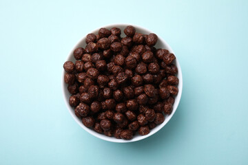 Chocolate cereal balls in bowl on light blue table, top view