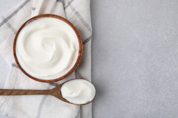 Delicious natural yogurt in bowl and spoon on light grey table, top view. Space for text