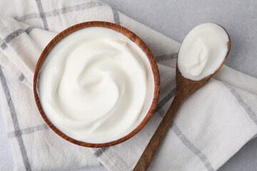 Delicious natural yogurt in bowl and spoon on light grey table, top view