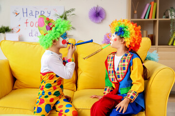 Funny little children in clown costumes with party whistles at home. April Fools' Day celebration