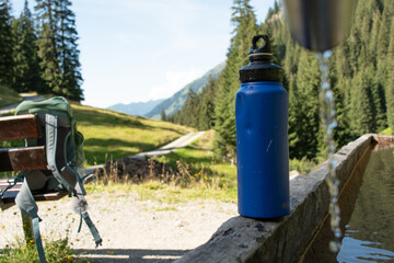 Fototapeta na wymiar Refilling Blue Water Bottle at Mountain Spring for Sustainable Travel