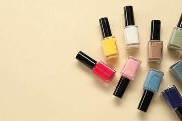 Obraz premium Colorful nail polishes in bottles on beige background, flat lay. Space for text