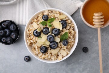Tasty oatmeal with blueberries, mint and almond petals in bowl on grey table, flat lay