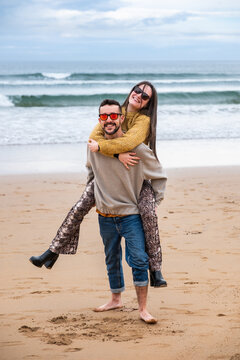 A young couple looking at camera while laughing and playing in the beach in winter.