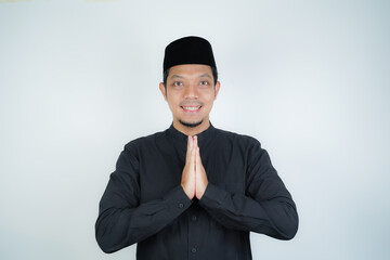 Happy smiling Asian Muslim man standing with Eid greeting gesture and welcoming Ramadan isolated background