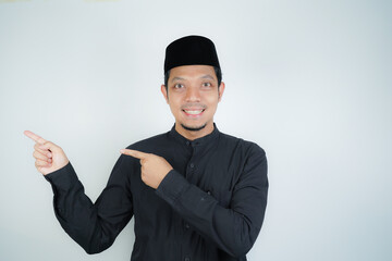 Obraz na płótnie Canvas Cheerful handsome Asian Muslim man pointing hand finger at empty space for advertising on isolated background