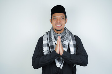 Obraz na płótnie Canvas Happy smiling Asian Muslim man in Arabic turban sorban standing with Eid greeting gesture and welcoming Ramadan isolated background