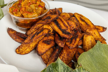 A plate of fried plantain or African Dodo with a bowl of spicy dip and banana leaves © SockaGPhoto