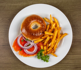 Top down view of a bagel with smoked salmon or lox and french fries and onion slice and capers